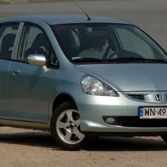 Jasnoszary Honda Jazz 2 z polskimi tablicami rejestracyjnymi WN 49746, zaparkowany przy wodzie.