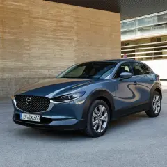 Szary Mazda CX-30 stoi przed betonową ścianą. Wady tego modelu to m.in. ograniczona widoczność z tyłu.