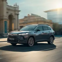 Nowy Toyota Corolla Cross 2025 w ciemnoszarym kolorze sunie po miejskiej ulicy, odbijając światło zachodzącego słońca.