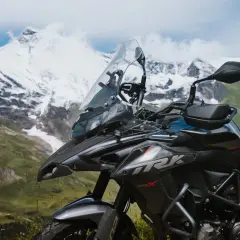 Ciemny motocykl turystyczny na tle ośnieżonych gór i zielonej doliny.