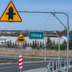 Znaki drogowe: pierwszeństwo przejazdu, przejazd kolejowy, nazwa miejscowości Elbląg.