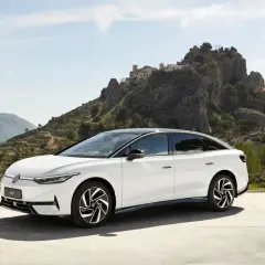 Biały Volkswagen ID.7 na tle malowniczego, skalistego krajobrazu z wioską na wzgórzu.
