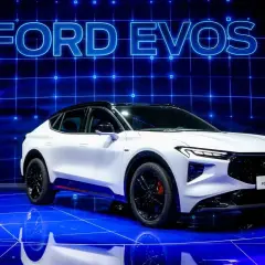 Biały Ford Evos na niebieskiej scenie z napisem "FORD EVOS" w tle.
