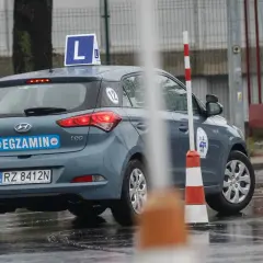 Szary Hyundai i20 z literą "L" na dachu i napisem "EGZAMIN" na klapie, gotowy do jazdy próbnej.