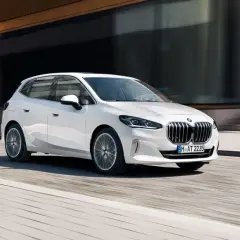 Białe BMW 218i sunie po miejskiej ulicy, odbijając światło od nowoczesnej fasady budynku.