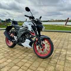 Stylowy japoński motocykl Suzuki GSX-S125 z czerwonymi felgami stoi na brukowanym placu nad jeziorem.