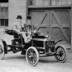 Dwóch dżentelmenów w melonikach siedzi w zabytkowym Fordzie Model T Runabout, gotowych na przejażdżkę.