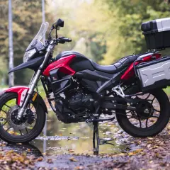 Czerwony motocykl turystyczny z kuframi, zaparkowany na jesiennej drodze. Model kat a1 gotowy na przygodę.