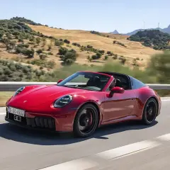 Czerwony Porsche 911 Carrera 4 GTS Targa sunie po krętej drodze wśród wzgórz.