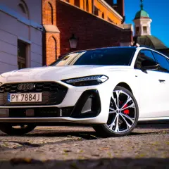Białe Audi A5 2025 z czerwonymi zaciskami hamulcowymi na tle zabytkowej architektury.