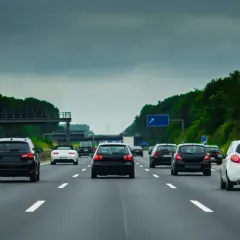 Samochody jadące drogą szybkiego ruchu pod pochmurnym niebem. W oddali widać zielone drzewa i wiadukt.