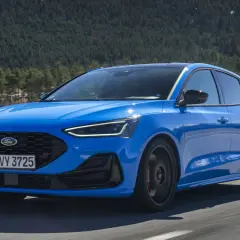 Niebieski Ford Focus ST na drodze, zalesione wzgórza w tle.