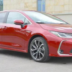 Czerwona Toyota Corolla 1.8 Hybrid z nowoczesnymi felgami stoi przed budynkiem.