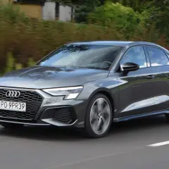 Szary Audi a3 sedan jedzie po drodze, otoczony zielenią.