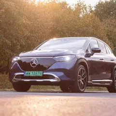 Elegancki, ciemnogranatowy Mercedes EQE SUV lśni w jesiennym słońcu na tle drzew.