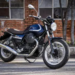 Stylowy, ciemnoniebieski motocykl Moto Guzzi V7 Special z chromowanymi elementami i szprychowymi kołami, zaparkowany przed ceglanym budynkiem.
