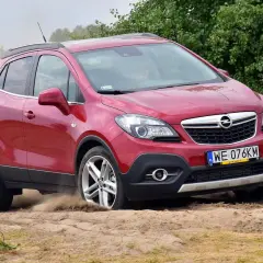 Czerwony Opel Mokka 2015 na piaszczystej drodze, unoszący kurz.