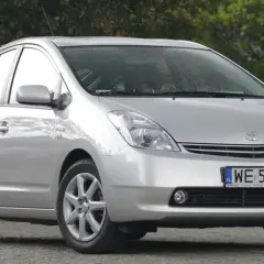 Srebrny Toyota Prius 2 zaparkowany przed ceglanym budynkiem.