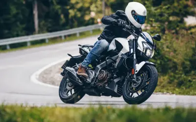 Motocyklista w białym kasku i czarnej kurtce pokonuje zakręt na drodze leśnej na motocyklu Bajaj Dominar 400.