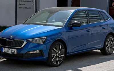 Błękitna Skoda Scala z czarnym dachem, zaparkowana przed budynkiem z napisem "Gebrauchtwagen".