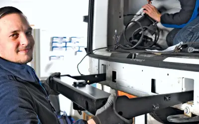 Uśmiechnięty mechanik z rękawicami montuje hak holowniczy do samochodu.