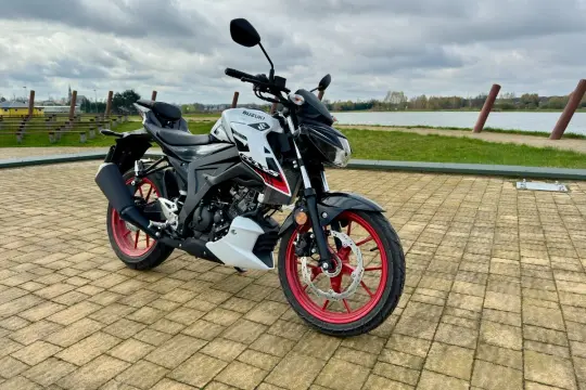 Stylowy japoński motocykl Suzuki GSX-S125 z czerwonymi felgami stoi na brukowanym placu nad jeziorem.