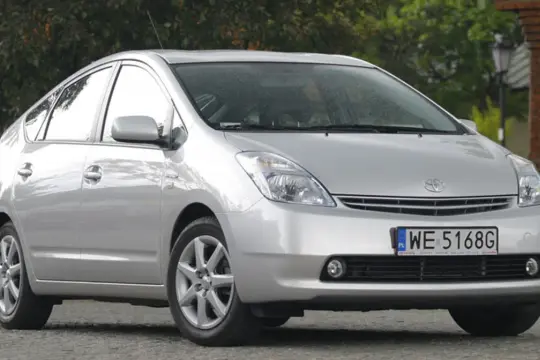 Srebrny Toyota Prius 2 zaparkowany przed ceglanym budynkiem.