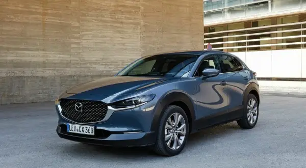 Szary Mazda CX-30 stoi przed betonową ścianą. Wady tego modelu to m.in. ograniczona widoczność z tyłu.