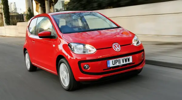 Czerwony Volkswagen up! pędzi ulicą, odbijając światła miasta w swoich lśniących powierzchniach.