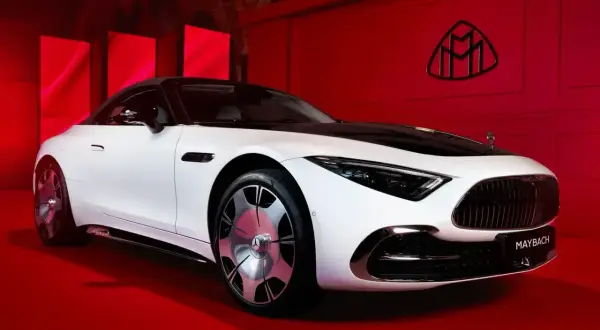 Elegancki biały Maybach z czarnym dachem na czerwonym tle. Logo Maybach widoczne na ścianie. Poznaj jego wyjątkową maybach cena.