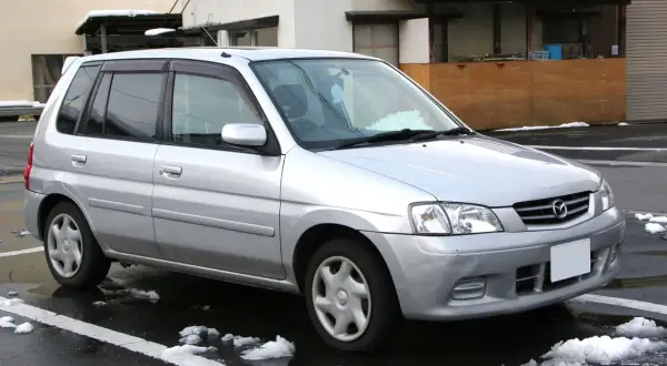Srebrna Mazda Demio zaparkowana na mokrej nawierzchni ze śniegiem.