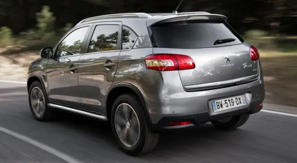 Srebrny Peugeot 4008 jedzie po drodze wśród drzew.