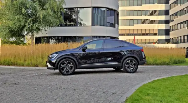 Elegancki, czarny Renault Arkana na tle nowoczesnych budynków. Zwróć uwagę na jego dynamiczne linie, które podkreślają jego sportowy charakter i optymalne renault arkana wymiary.