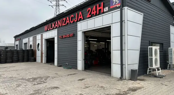 Budynek wulkanizacji z napisem "Wulkanizacja 24H", stosy opon i otwarte bramy garażowe.
