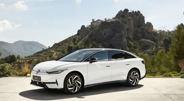 Biały Volkswagen ID.7 na tle malowniczego, skalistego krajobrazu z wioską na wzgórzu.