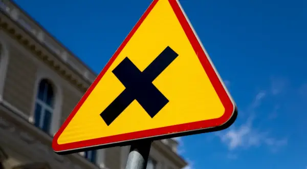 Żółty trójkąt z czarnym znakiem "X" ostrzega o skrzyżowaniu dróg. Uważaj, bo to droga z pierwszeństwem.