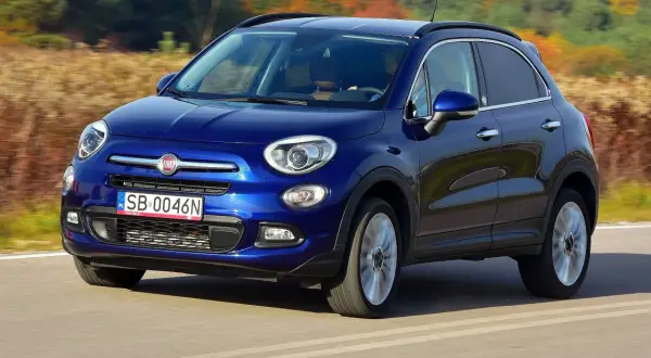 Niebieski Fiat 500 XL jedzie po drodze, otoczony jesiennym krajobrazem.