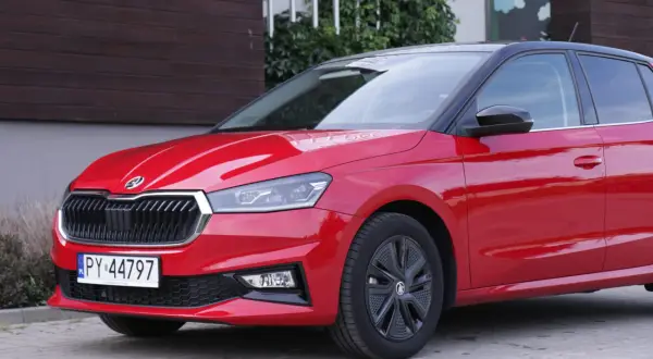 Czerwona Skoda Fabia 4 z czarnym dachem i felgami stoi przed budynkiem.