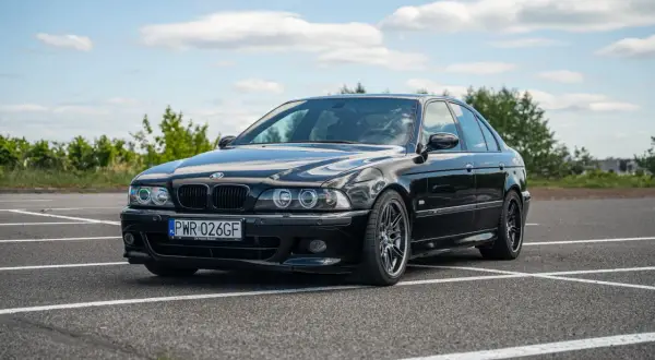 Czarne BMW E39 na parkingu, z widocznym przodem i bokiem samochodu.