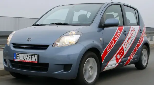 Niebieski Daihatsu Sirion z napisem "AUTO CLUB DAIHATSU" na boku, jadący po drodze.