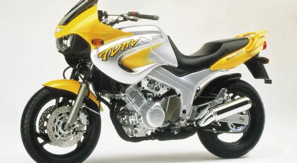 Żółto-srebrny motocykl Yamaha TDM 850 z charakterystycznym malowaniem "TDM" na baku. Gotowy na przygodę!