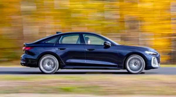 Ciemnoniebieskie Audi A4 B10 w ruchu, z rozmytym tłem jesiennych drzew.