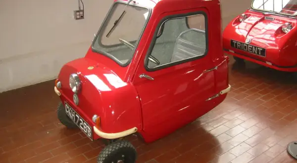 Czerwony, trójkołowy samochód Peel P50, najmniejszy pojazd na świecie, stoi na ceglanej podłodze.
