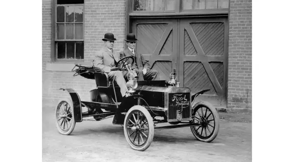 Dwóch dżentelmenów w melonikach siedzi w zabytkowym Fordzie Model T Runabout, gotowych na przejażdżkę.
