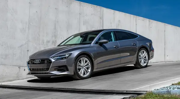 Elegancki, szary Audi A7 2025 z panoramicznym dachem stoi na tle betonowej ściany.