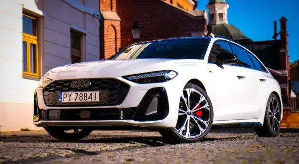 Białe Audi A5 2025 z czerwonymi zaciskami hamulcowymi na tle zabytkowej architektury.