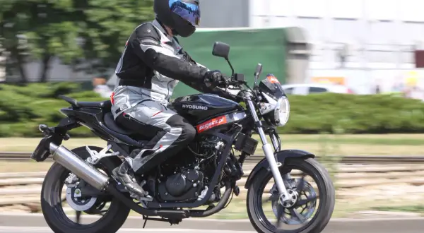 Motocyklista w pełnym stroju pędzi na czarnym Hyosung GT 125, ciesząc się jazdą.