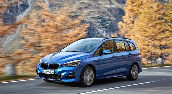 Niebieskie BMW 2 Gran Tourer jedzie po górskiej drodze jesienią.