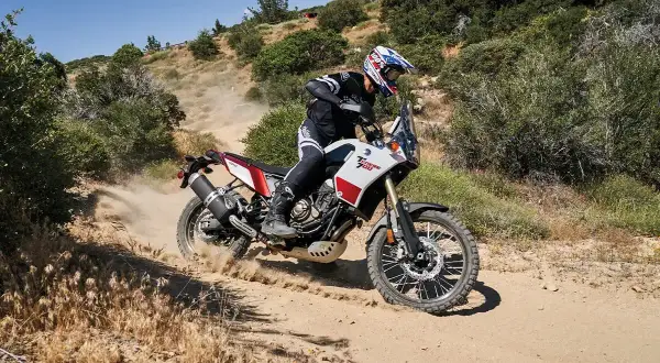 Motocyklista na motocyklu Yamaha Tenere 700 pokonuje piaszczysty zakręt, wzbijając tumany kurzu.
