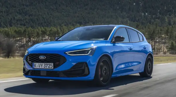 Niebieski Ford Focus ST na drodze, zalesione wzgórza w tle.